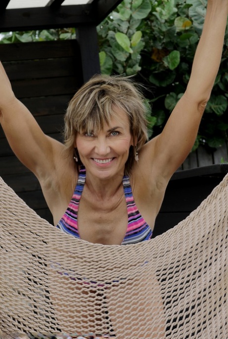 Mature woman Lillian Tesh fingers her pussy on a hammock after bikini removal