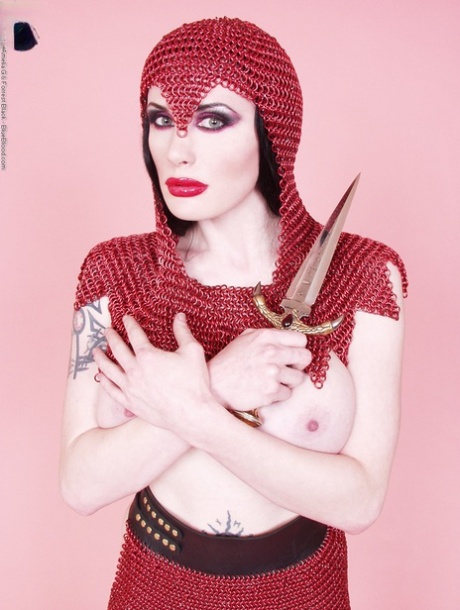 Busty chick Morrigan Hel licks a dagger while wearing chain mail and OTK boots