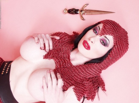 Busty chick Morrigan Hel licks a dagger while wearing chain mail and OTK boots