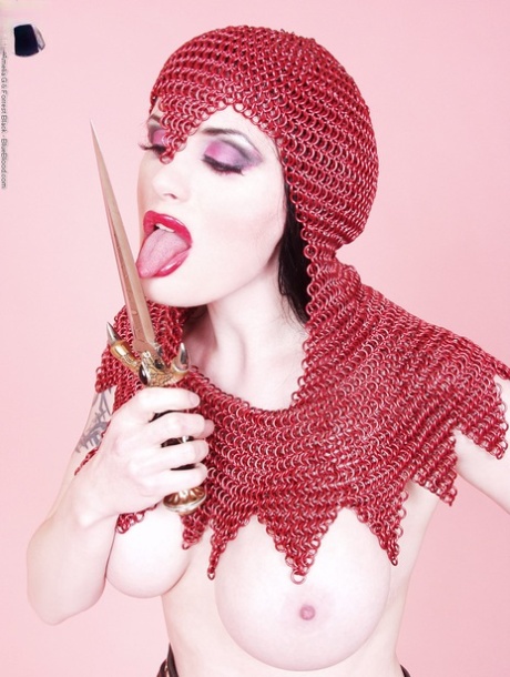 Busty chick Morrigan Hel licks a dagger while wearing chain mail and OTK boots