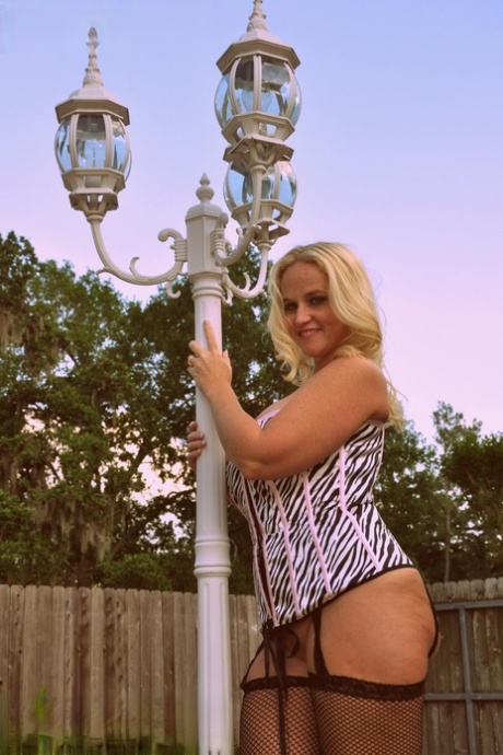 Blonde amateur Dee Siren models a laced corset and mesh hosiery in a backyard