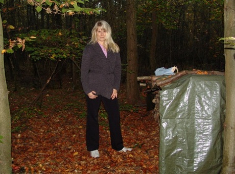 Mature blonde Sweet Susi shows her naked ass by a stack of firewood