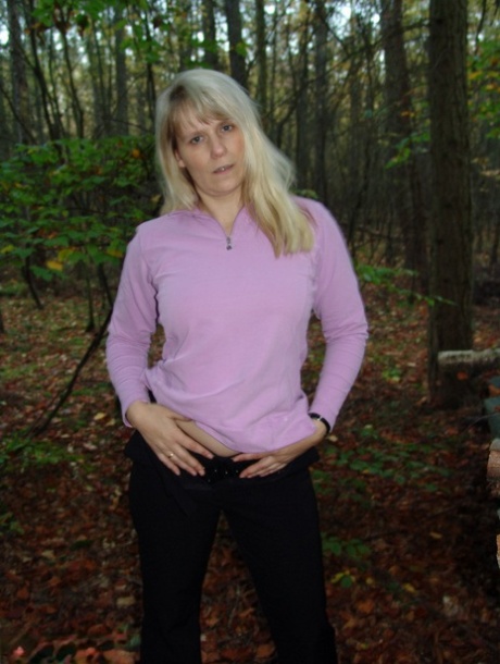 Mature blonde Sweet Susi shows her naked ass by a stack of firewood