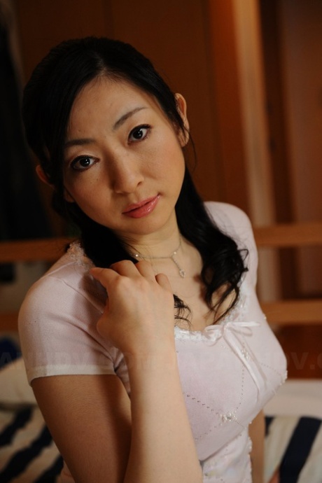 Slender mature Japanese woman Emiko Koike bends over to pose in white dress