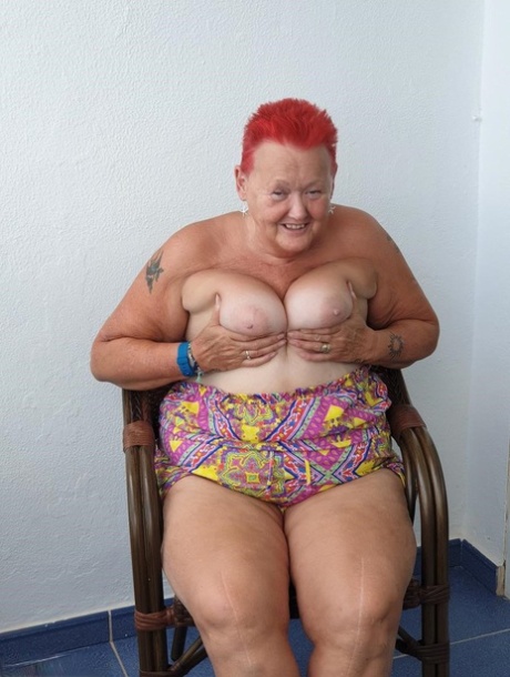 Obese nan with spiky red hair unveils her tits on balcony before posing naked