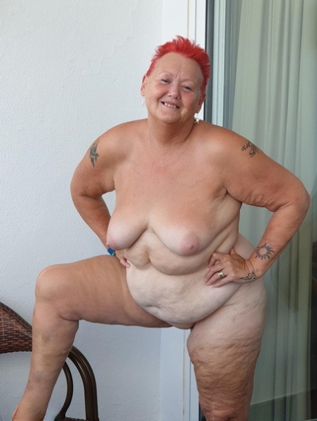 Obese nan with spiky red hair unveils her tits on balcony before posing naked
