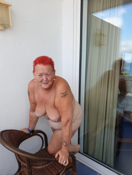 Obese nan with spiky red hair unveils her tits on balcony before posing naked