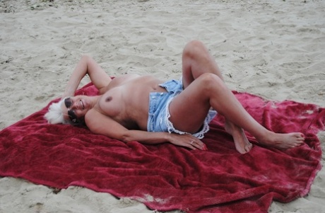 Mature blonde Dimonty eats a frozen treat after posing nude on a beach