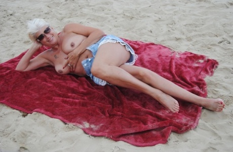 Mature blonde Dimonty eats a frozen treat after posing nude on a beach