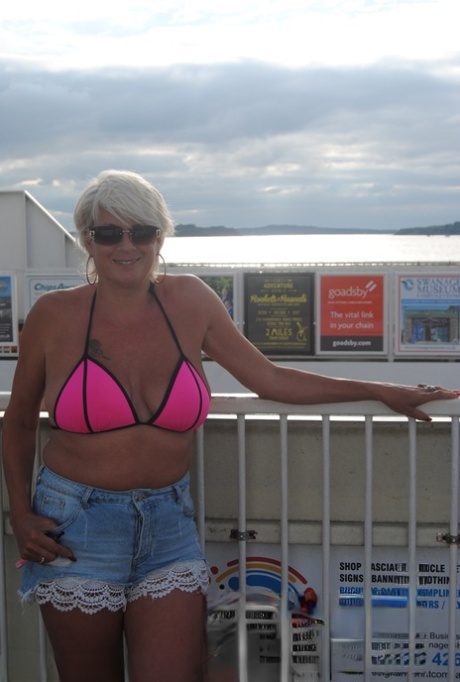 Mature blonde Dimonty eats a frozen treat after posing nude on a beach