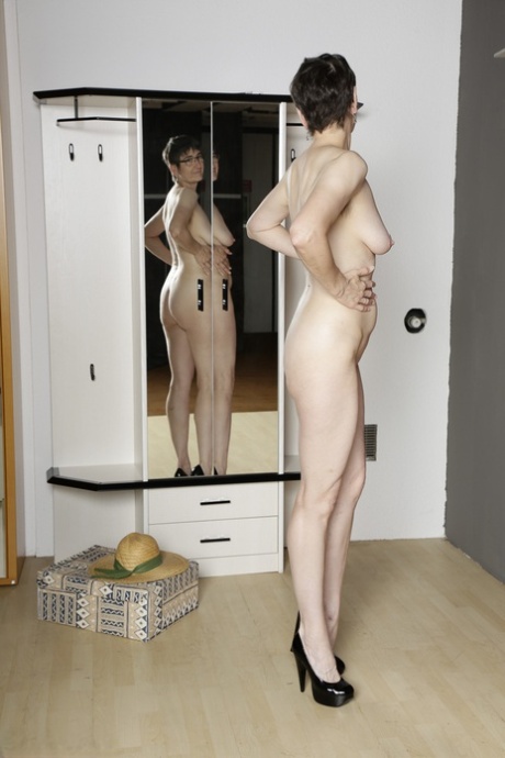 Mature amateur admires her naked body in a mirror while wearing black heels