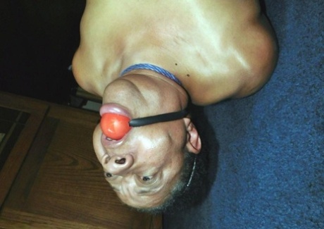 Overweight black woman Trixie struggles against a ball gag while hogtied