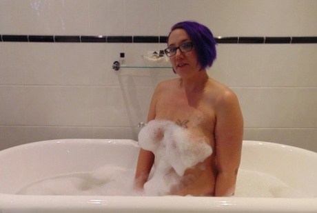 Mature plumper Sara Banks sports dyed hair while taking a bubble bath