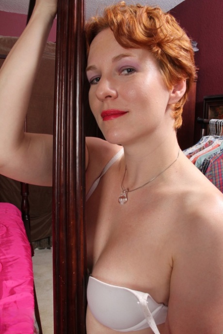 Redhead American housewife removes her clothes and toys her pussy on the bed
