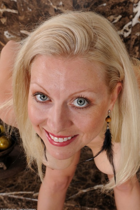 Blonde mature Zoey Tyler exposes her big tits and tasty muff by the fireplace
