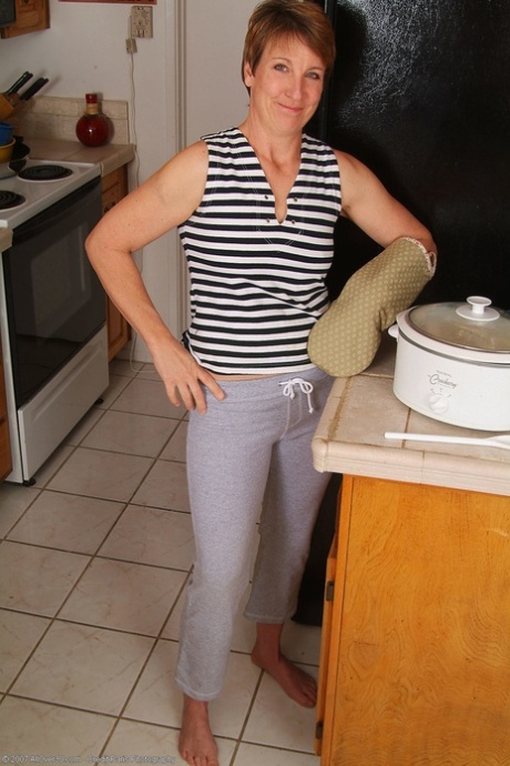 Skinny mature with short hair Embers undresses and poses nude in the kitchen