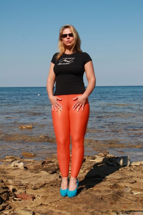Hot MILF Desyra Noir reveals her big tits as she strips to her latex leggings